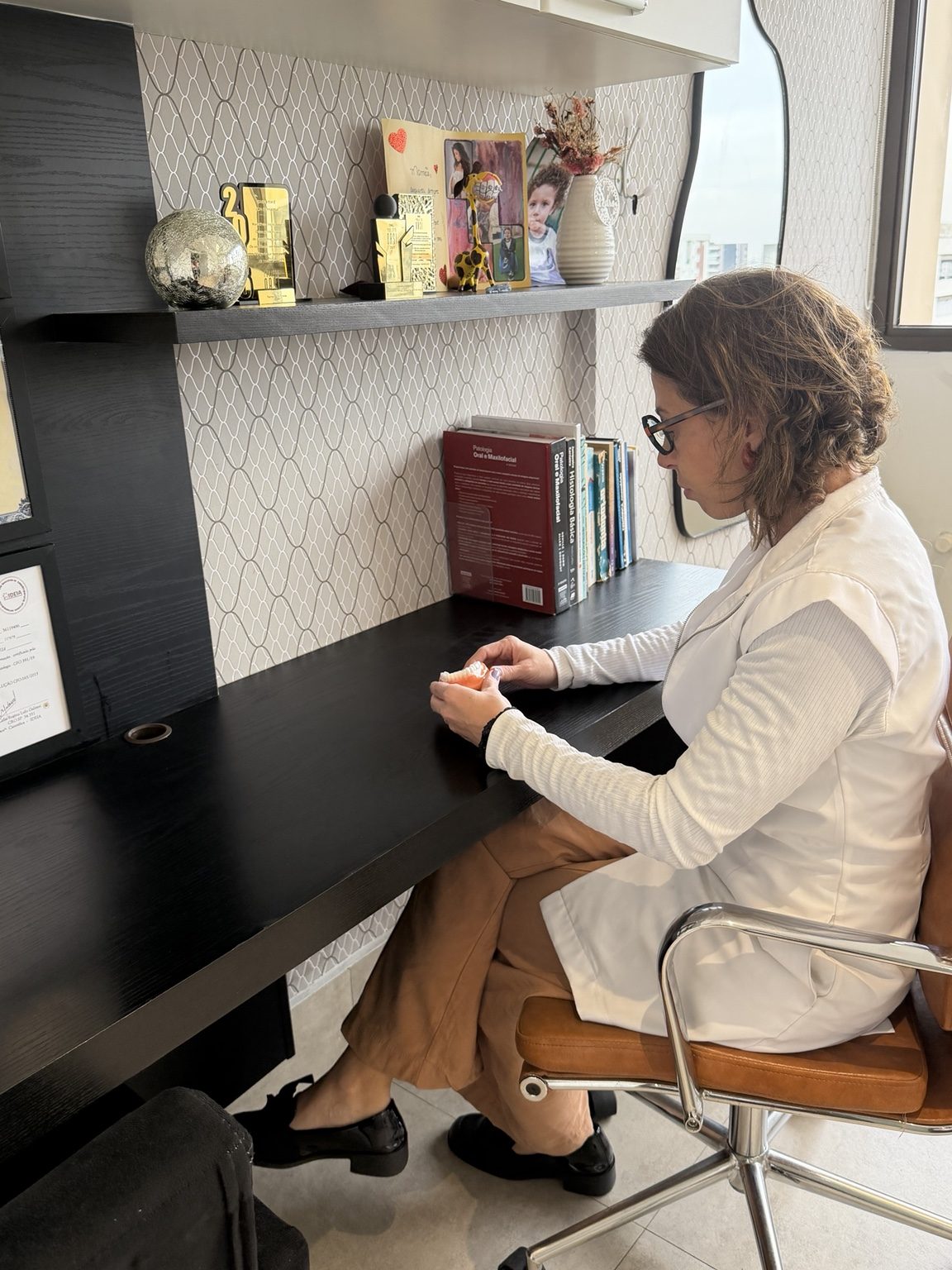 Dra. Camila Meira analisando um modelo odontológico em sua mesa de trabalho