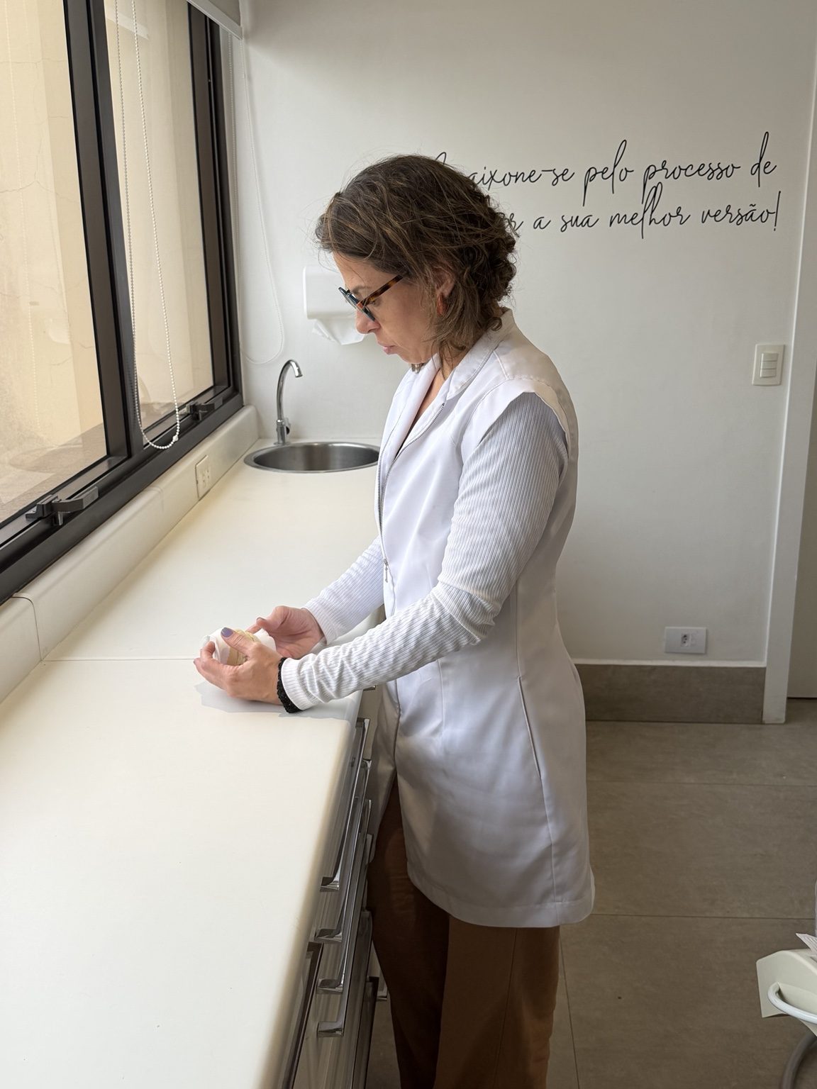 Dra. Camila Meira examinando um modelo odontológico próximo à janela do consultório